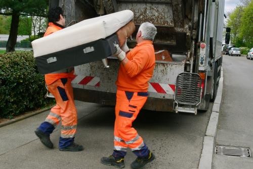 zwei Müllwerker die ein Sofa in das Sperrmüllfahrzeug laden