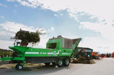 Mobiler Häcksler, der mittels eines Radladers mit Baum- und Heckenschnitt befüllt wird