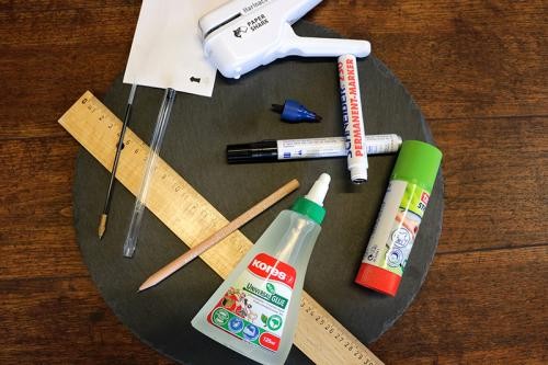 Büromaterialien wie Kleber, Holzlineal, Stifte und Papierhefter ohne Metallklammern