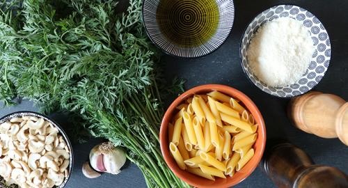 Möhrengrün und Schüsseln mit Nudeln, Öl, Nüssen, Parmesan und Cashewkernen