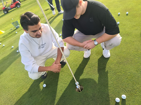 Golftrainer mit einem Jugendlichen auf dem Golfplatz beim Besprechen