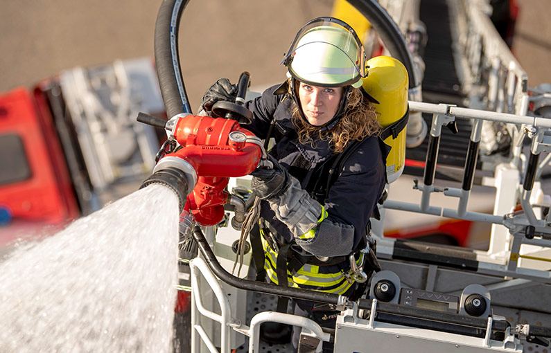 Feuerwehrfrau im Korb auf der Drehleiter mit Schlauch aus dem Wasser schießt