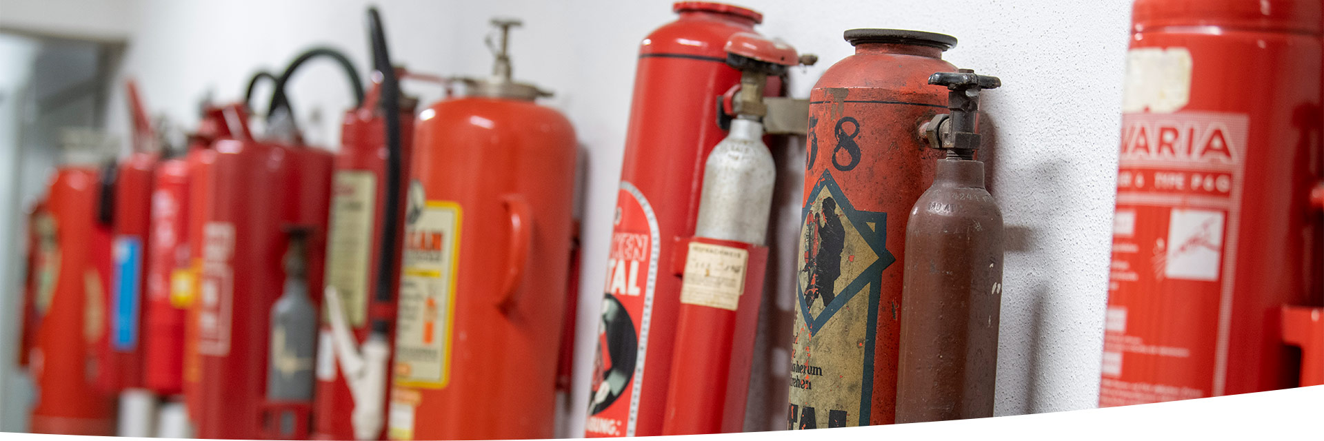 Verschiedene Feuerlöscher hängen nebeneinander an einer Wand