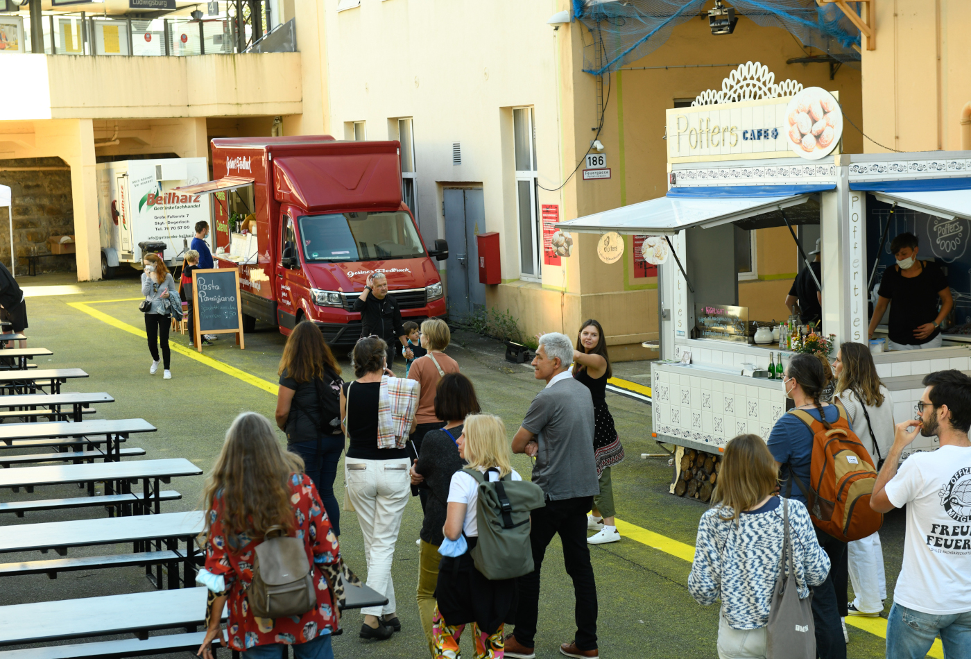 Eine Gruppe Menschen läuft über das Areal an zwei Foodtrucks vorbei.