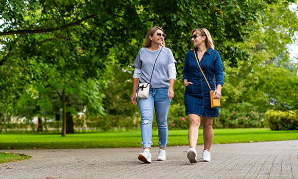 Zwei Frauen gehen nebeneinander auf einem Fußweg im Park.