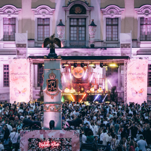 Viele Menschen tanzen im Innenhof des Residenzschlosses vor einer Bühne. Die Schlossfassade ist lila beleuchtet