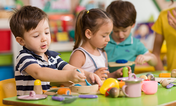 Drei Kinder sitzen an einem Tisch und spielen.