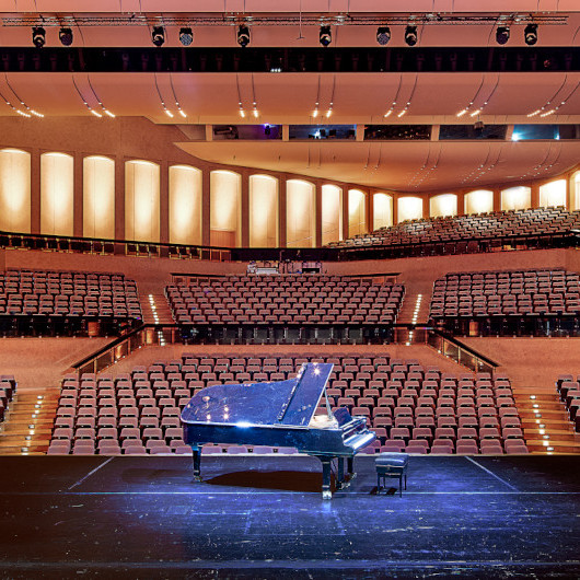 Ein Flügel steht auf der Bühne im Schlosspark, im Hintergrund sieht man den Theatersaal