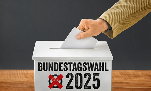 Symbolbild: Hand steckt Stimmzettel in Urne mit der Aufschrift "Bundestagswahl 2025"