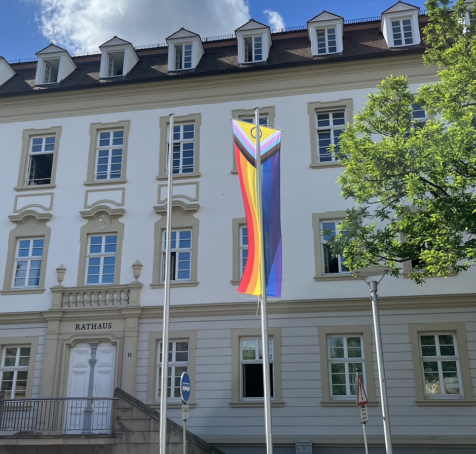 Die gehisste Progressive Pride Flag vor dem Eingang des Rathauses.