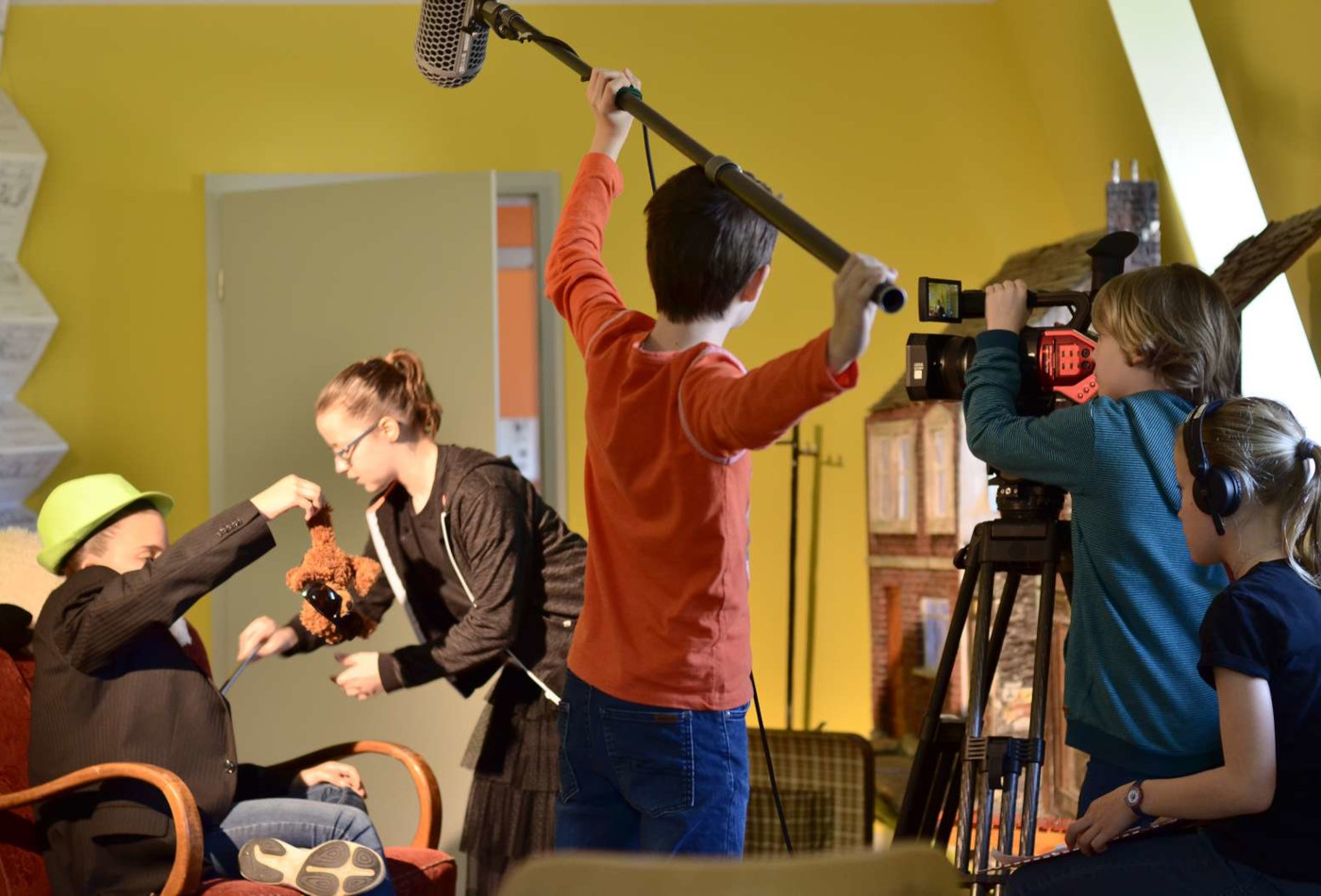 Mehrere Kinder sind in ein Filmset involviert mit Kamera und Mikrofon.
