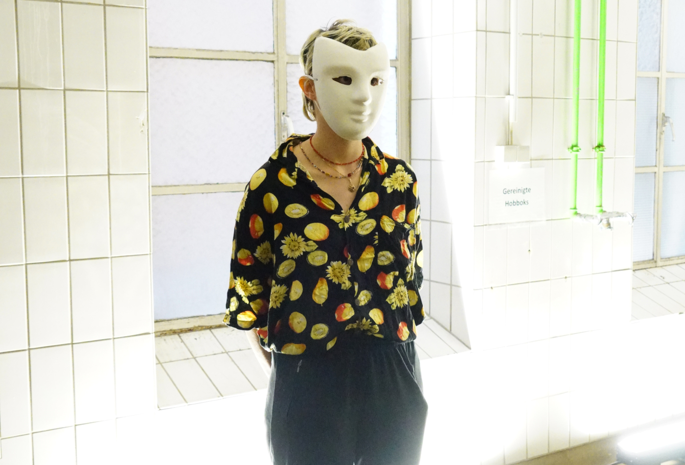 Eine Person mit einer weißen Maske steht in einem gekachelten Raum