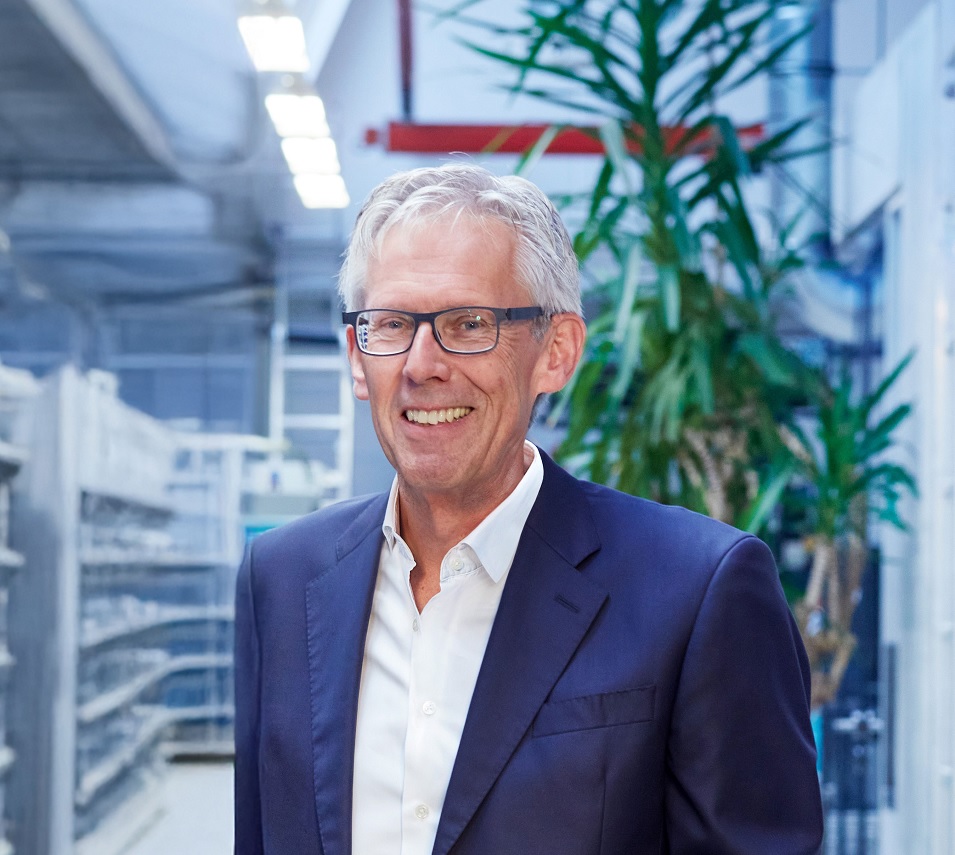Der Geschäftsführer Detflef Weimann steht im Produktionsbereich des Unternehmens. Er trägt Brille, ein weißes Hemd und einen dunklen Anzug.      