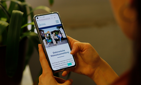 Person schaut auf Smartphone, auf dem die Seite der digitalen Wohnungsanmeldung geöffnet ist.