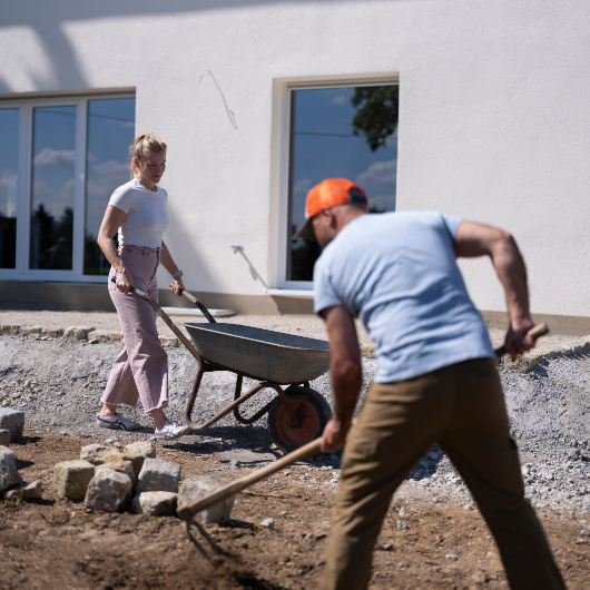 Frau und Mann mit einer Schubkarre und einer Harke
