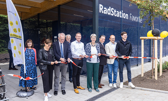 Mehrere Personen zerschneiden ein Absperrband. Hinter ihnen befindet sich die Radstation Favorite.