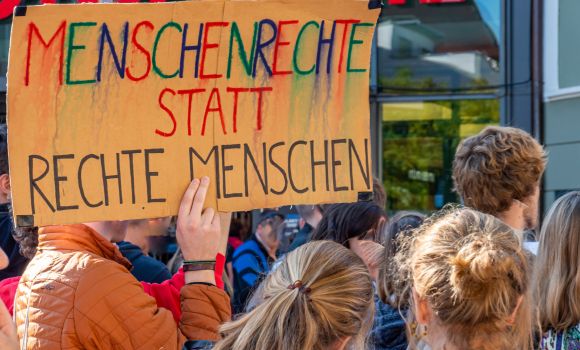 Menschen bei Demo. Ein Mann hält ein Schild mit der Aufschrift "Menschenrechte statt rechte Menschen" hoch.