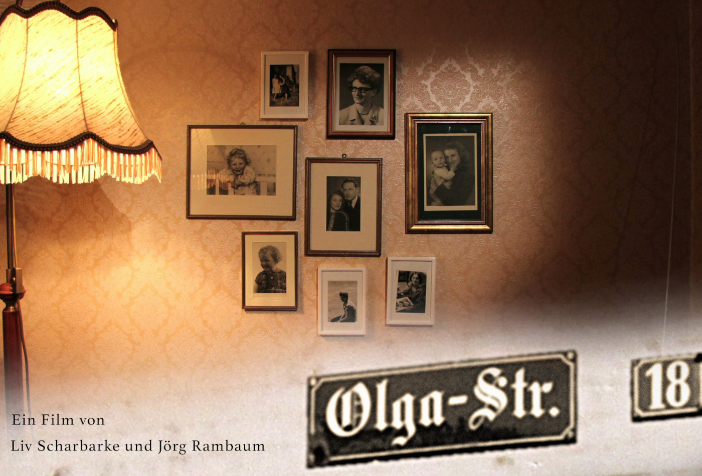 Neben einer alten Stehlampe hängen alte schwarz-weiß Fotos an einer Wand.