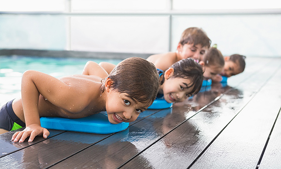 Kinder am Rand eines Schwimmbeckens mit Schwimmbrettern.