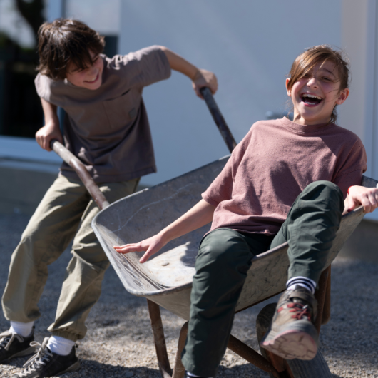 Zwei lachende Kinder mit einer Schubkarre