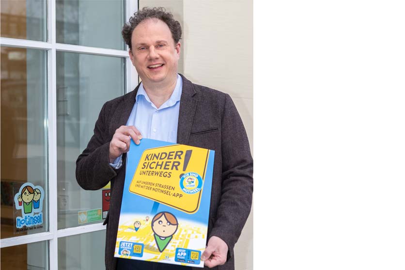 Ein Mann steht vor einer Glastür mit einem Plakat in den Händen. Auf der Glastür ist ein Aufkleber zu erkennen. 