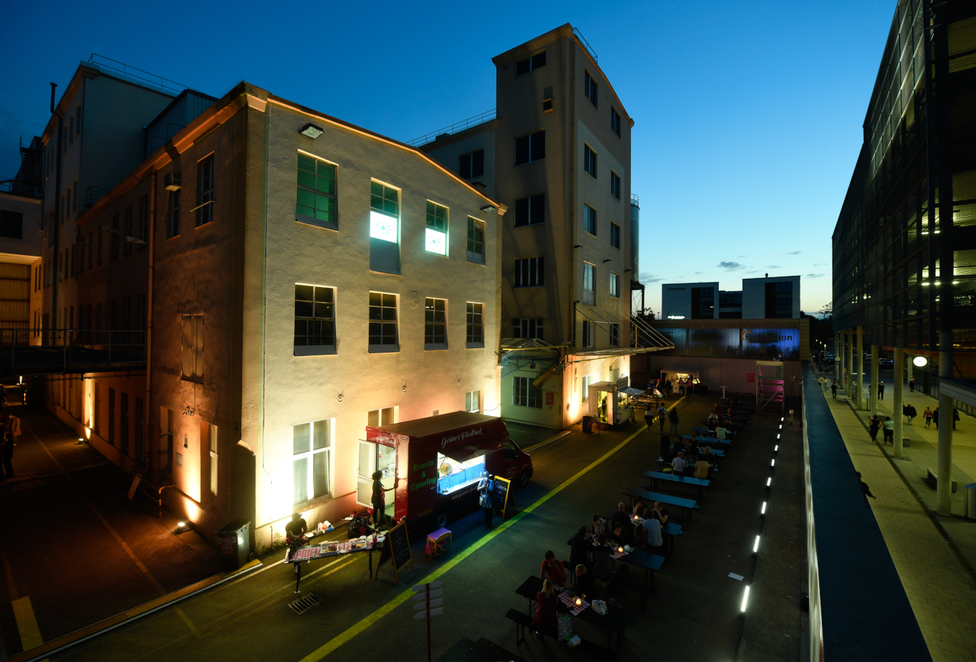 Der Außenbereich mit Gastronomie strahlt im dunkler werdenden licht der Abendsonne.
