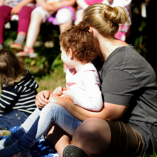 Frau hat Kind auf dem Schoß sitzen und umarmt es liebevoll