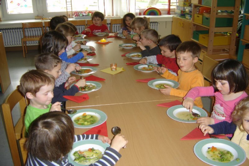 Kinder sitzen am Tisch und essen gemeinsam Gem&uuml;sesuppe 