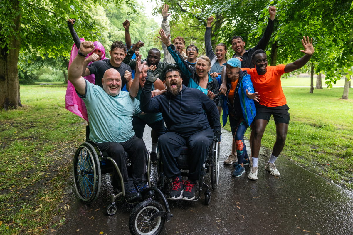 Gruppenbild mit mehrern Personen im Park mit 2 Rollstuhlfahrern im Vordergrund